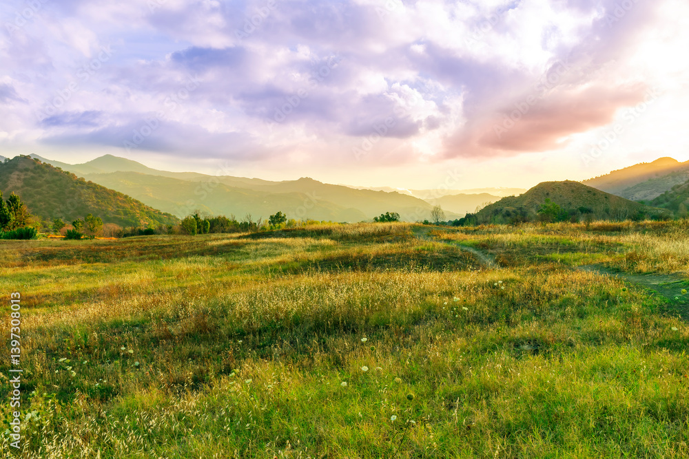 Fototapeta premium beautiful green valley with green fields with green spring grass with nive hills and mountains and scenic colorful cloudy sunset on background of landscape