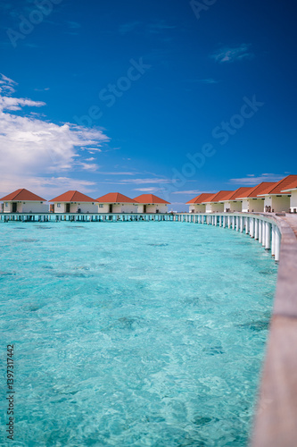 Fototapeta Naklejka Na Ścianę i Meble -  Luxury overwater villas with red rooftops above crystal clear turquoise lagoon under deep blue sky in tropical island resort.