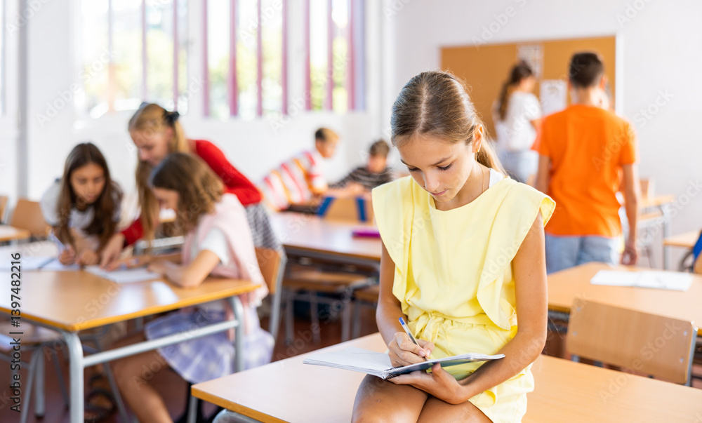 Portrait of schoolgirl with notebook in her hands who sits on desk in a school class Portrait of schoolgirl with notebook in her hands who sits on desk in a school class