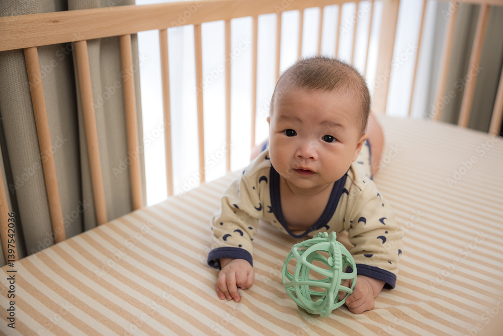 Baby turning and crawling on bed with play ball