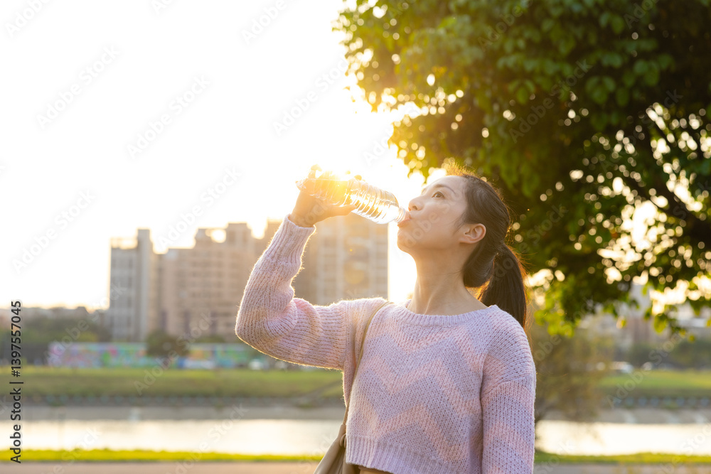 Young Woman Drinking Water Near River At Sunset