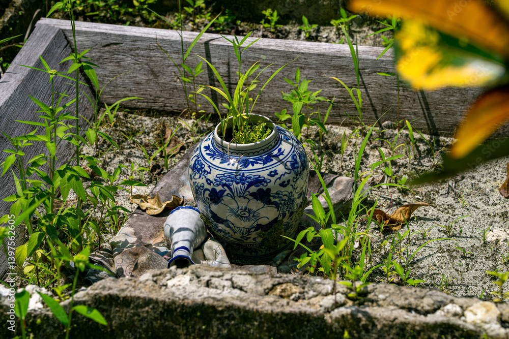Fototapeta premium Blue floral ceramic jar with grass growing from inside placed in sandy garden