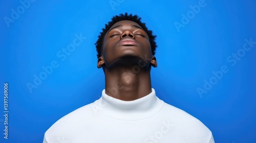 Close-up portrait of a young man with eyes closed, head tilted back, against a vibrant blue background, wearing a white turtleneck