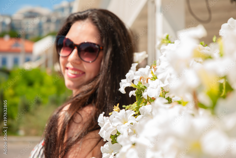 Smiling woman in sunglasses enjoying a sunny day surrounded by white flowers. Happy summer days, travel and vacation concept Smiling woman in sunglasses enjoying a sunny day surrounded by white flowers. Happy summer days, travel and vacation concept
