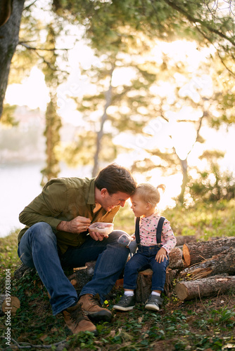 Dad leaned his forehead against the forehead of a little girl sitting with her on logs in the forest
