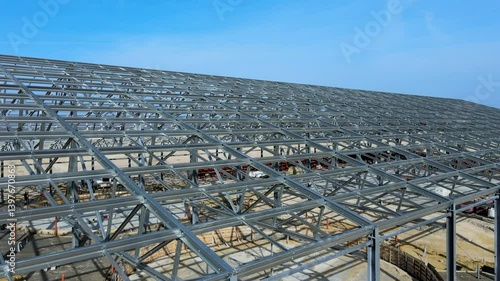 Flight past the large metal building structure is taking shape in an agricultural zone. Metal frames are installed, creating an expansive space for future cultivation growth or animal husbandry