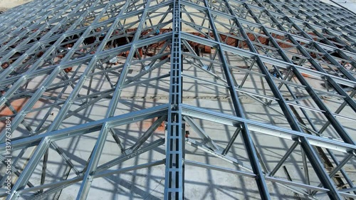 Flight over large metal building structure is taking shape in an agricultural zone. Metal frames are installed, creating an expansive space for future cultivation growth or animal husbandry