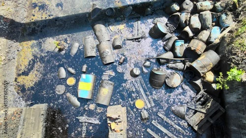An abandoned industrial site shows waste and debris scattered amid overgrown vegetation. The polluted bitumen area highlights the impact of neglect on the environment