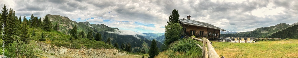 Panoramic mountain cabin view with lush greenery and a cloudy sky Panoramic mountain cabin view with lush greenery and a cloudy sky