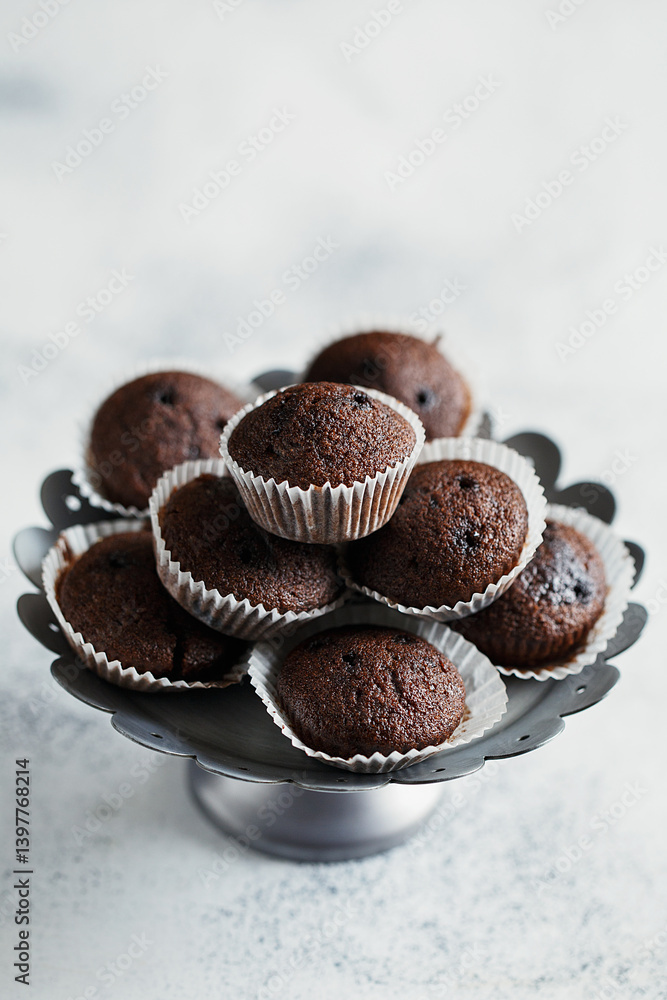 Close up view of cake stand with small chocolate muffins or cupcakes on white concrete background. Side view Close up view of cake stand with small chocolate muffins or cupcakes on white concrete background. Side view