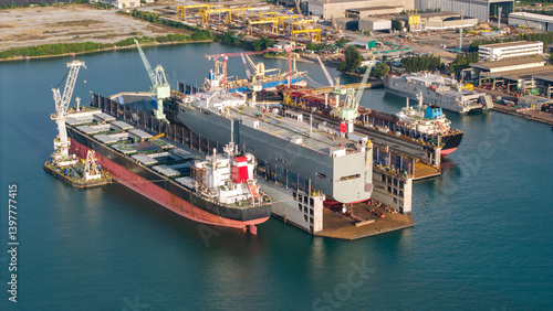 Aerial view of a shipyard repairing a large ship maintenance or repair at floating dock in shipyard both deck crane loading during bring ship in to the dry dock.