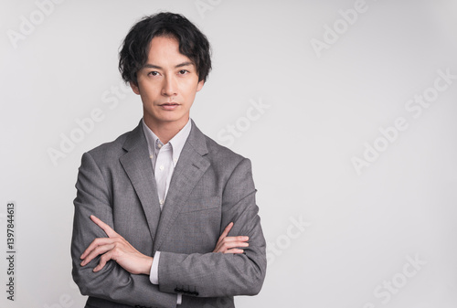スーツを着ている男性が腕組みをしている。/ジェスチャー/スタジオ撮影グレー背景