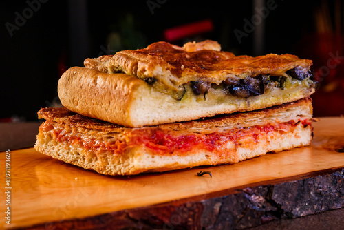 Due parigine napoletane ripiene con pomodoro, prosciutto e provola e con scarole, olive e acciughe servite in una rosticceria su un tagliere di legno