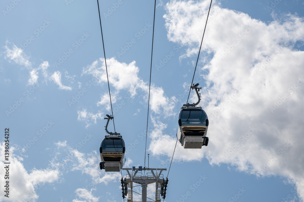Cable Cars Ascending: Capturing the Skyward Journey of Modern Transportation, two cable cars ascend against a beautiful backdrop of fluffy clouds and a vibrant blue sky. Cable Cars Ascending: Capturing the Skyward Journey of Modern Transportation, two cable cars ascend against a beautiful backdrop of fluffy clouds and a vibrant blue sky.