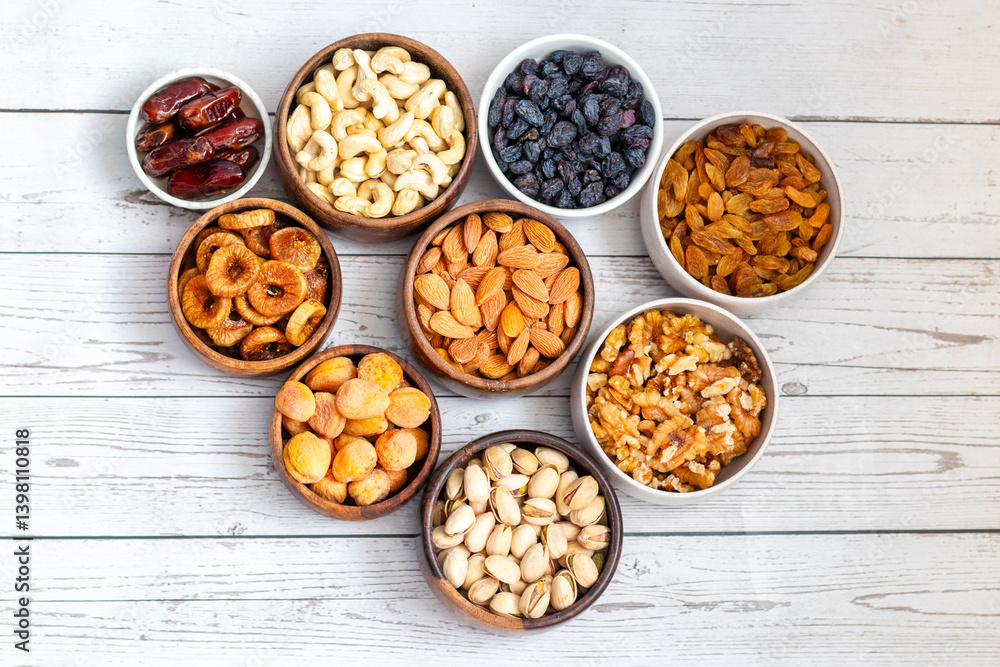 an assortment of dried fruits and nuts arranged in bowls on a white wooden surface, including dates, cashews, almonds, raisins, figs, apricots, and walnuts. an assortment of dried fruits and nuts arranged in bowls on a white wooden surface, including dates, cashews, almonds, raisins, figs, apricots, and walnuts.