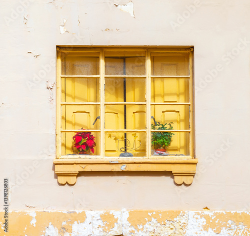 A yellow window with closed shutters behinde the frame