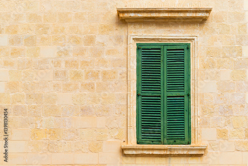 Stone brick wall with a closed green wooden window with shutters