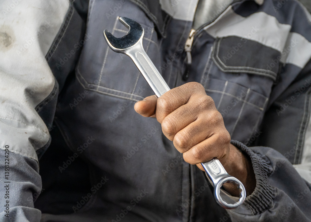 An African-American car mechanic holds a wrench in his hands in close-up, selective focus. Close up of a man's hand holding a wrench. A mechanic with a wrench after working with the car. An African-American car mechanic holds a wrench in his hands in close-up, selective focus. Close up of a man's hand holding a wrench. A mechanic with a wrench after working with the car.