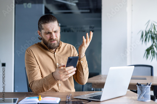Foto A frustrated man holds a smartphone, seemingly confused or exasperated while sitting at a desk