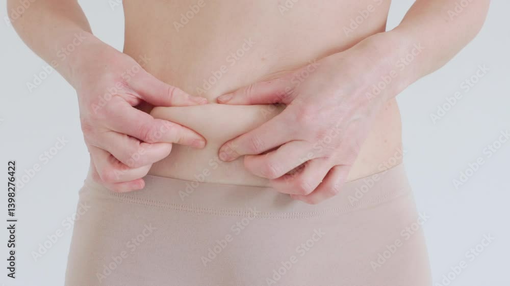 Close up of female belly with loose skin Woman pinches skin to show body fat and signs of aging Loss of elasticity and soft tissue Close up of female belly with loose skin Woman pinches skin to show body fat and signs of aging Loss of elasticity and soft tissue