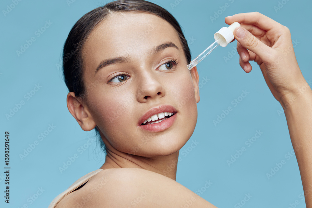 Young woman applying serum to her face, showcasing clear skin and a radiant smile against a soft blue background, emphasizing skincare and beauty Young woman applying serum to her face, showcasing clear skin and a radiant smile against a soft blue background, emphasizing skincare and beauty
