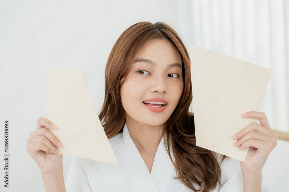 Asian teenage girl smiling gently while holding two blank papers wearing spa robe expressing skincare brightness freshness glow youth beauty concept in wellness lifestyle light and clean environment Asian teenage girl smiling gently while holding two blank papers wearing spa robe expressing skincare brightness freshness glow youth beauty concept in wellness lifestyle light and clean environment