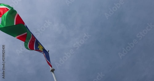 The National Flag of Namibia flutters in the wind. Great for news. Close-up. The Namibian flag against the blue sky. 4K video.