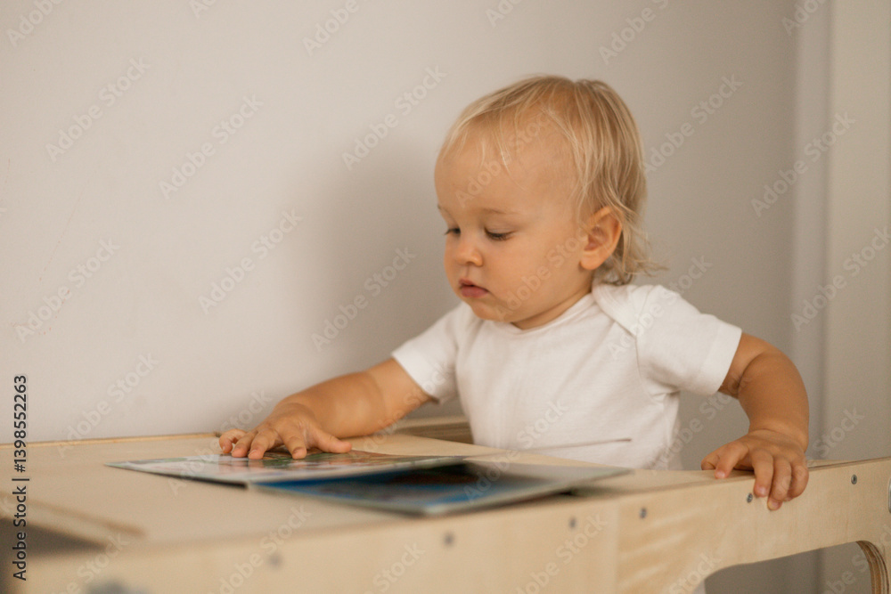baby girl looking at a book sitting at a wooden table
