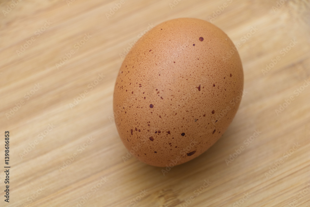 A brown egg with speckles on it is sitting alone on the wooden table, creating an overhead view. A brown egg with speckles on it is sitting alone on the wooden table, creating an overhead view.
