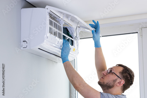 Professional Service: An Expert Technically Skilled Individual Reaches Up to Perform Maintenance on a Wall-Mounted Air Conditioning Unit for Optimal Performance and Longevity
