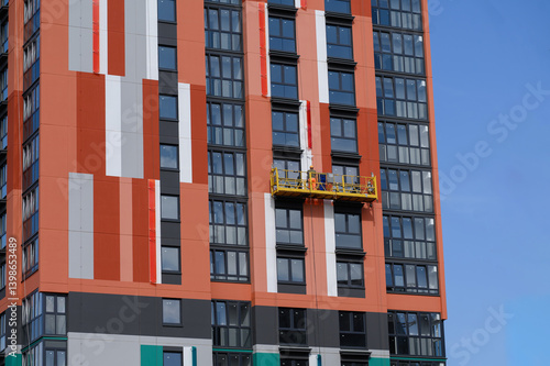 Worker is engaged in external works, insulation of house, renovation paints building, standing on cradle of facade lift. Concept of reconstruction and repair works of building