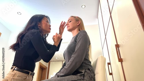 Professional makeup artist working with model, applying foundation and cosmetics in a modern home studio. The interaction showcases the process of a makeup session in progress