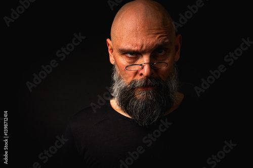 Obraz na płótnie Intense bald man with a grey beard and round glasses making a small pinch gesture. Low key portrait with dramatic lighting and expressive face on black background w salonie