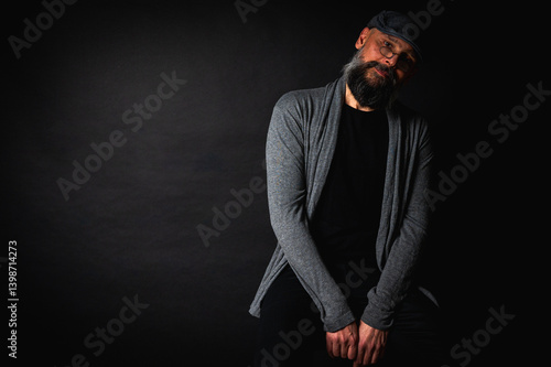 Obraz na płótnie Portrait of an emotional bearded man in a gray brass knuckles, a gray sweater and glasses looking at the camera on a dark background. Dramatic portrait in subdued lighting, expressive face, emotional w salonie