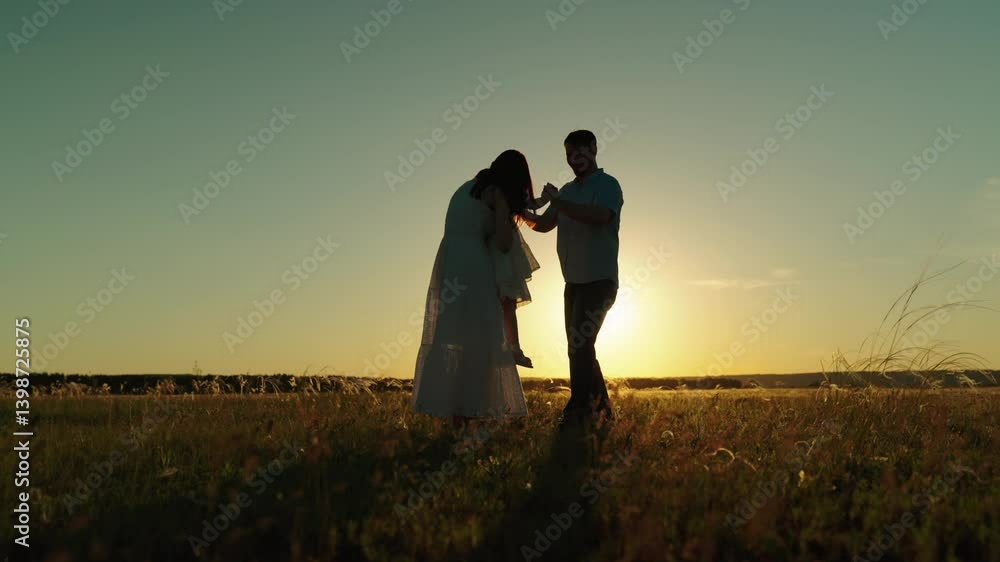 Happy family leisure on field with fun and joy feeling togetherness at sunset. Father spins daughter and gives kid to dancing mother hugs. Family dreamy flight of childhood at evening darkness Happy family leisure on field with fun and joy feeling togetherness at sunset. Father spins daughter and gives kid to dancing mother hugs. Family dreamy flight of childhood at evening darkness