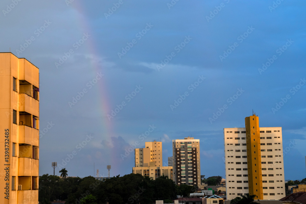 Rainbow over cityscape. Urban buildings under a colorful arc in the sky. Serene scene, perfect for illustrating city life and weather phenomena
