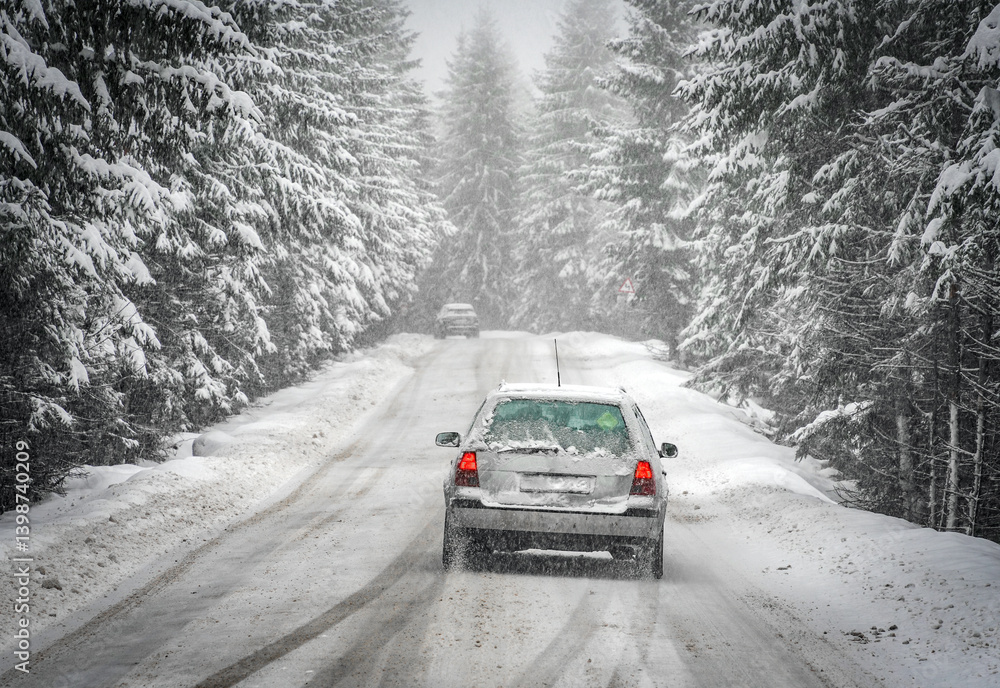 Beautiful winter scene with icy slick road driving car . Alpine road covered with water and ice and snowy trees all around
