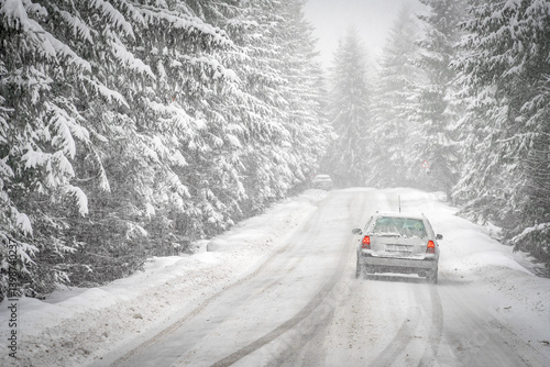 Winter scene with icy slick road driving car . Alpine road covered with water and ice and snowy trees all around	