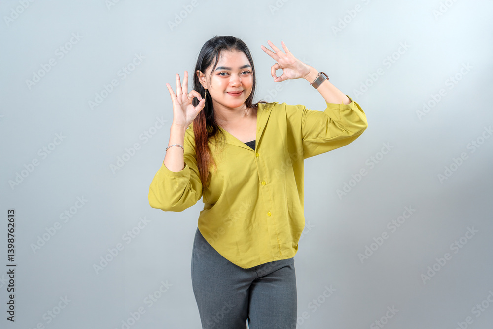 Confident young Asian woman smiling while making an OK hand gesture. Her bright expression and direct eye contact convey approval, assurance, and positivity for promotional use. Confident young Asian woman smiling while making an OK hand gesture. Her bright expression and direct eye contact convey approval, assurance, and positivity for promotional use.