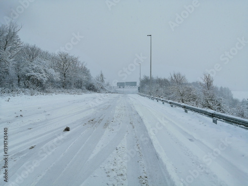 A snow-covered road winds through a winter landscape with trees on both sides during a winter storm.