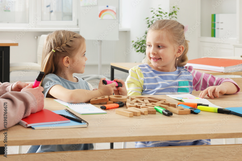 Fototapeta premium Children learning letters with teacher at desk indoors
