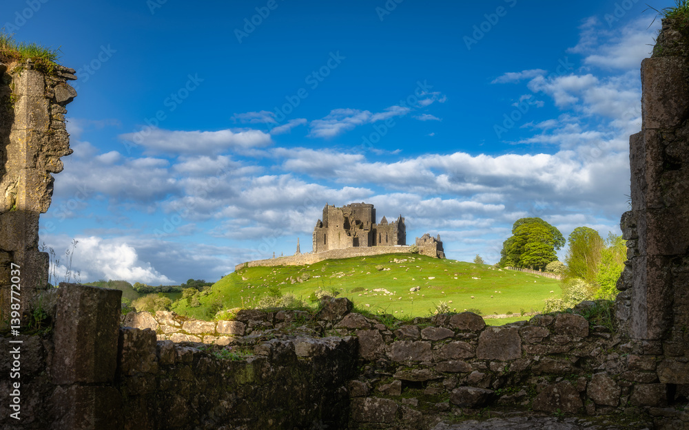 The Rock of Cashel castle ruins atop a hill, surrounded by ancient stone walls of Hore Abbey are enhanced by vibrant green grass and fluffy clouds creating a breathtaking landscape, Tipperary, Ireland