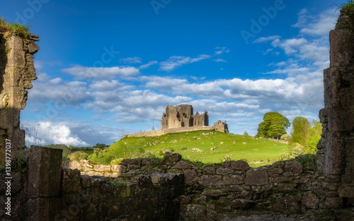 The Rock of Cashel castle ruins atop a hill, surrounded by ancient stone walls of Hore Abbey are enhanced by vibrant green grass and fluffy clouds creating a breathtaking landscape, Tipperary, Ireland