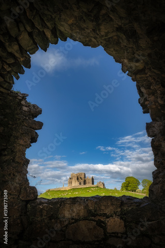 Obraz na płótnie Picturesque view of ancient historic ruins of Rock of Cashel, framed beautifully by stone arch of Hore Abbey, with striking clear blue skies and rolling green hills in the distance, Tipperary, Ireland w salonie