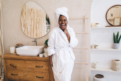 Obraz na płótnie Beautiful positive moment of pure happiness during morning routine. Portrait of cheerful dark skinned woman in white bathrobe and towel expressing genuine joy and expression in bathroom w salonie