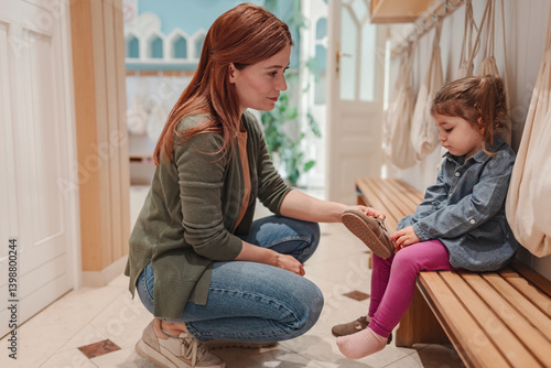 Preschool teacher kneels to talk kindly with a young girl in the changing area, offering comfort and support in a warm, nurturing early childhood setting.