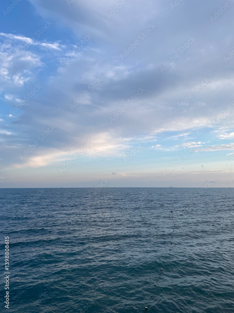 A tranquil landscape showcases a vast expanse of ocean water reflecting the sky. Gentle waves roll towards the shore, creating a calming atmosphere just before twilight