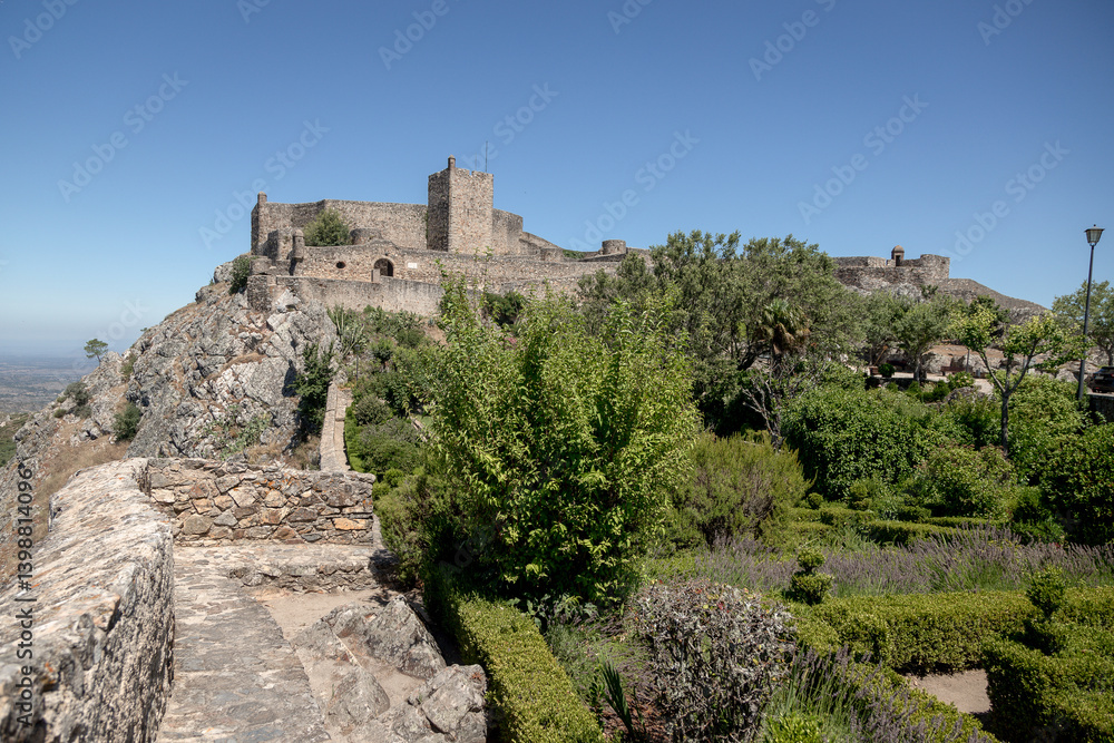 Obraz premium The medieval castle of Marvão, Portugal, stands atop a rocky cliff surrounded by gardens and ancient walls. Photographed on a clear summer day, this national monument overlooks the Alentejo plains.