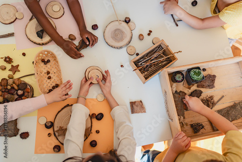 Multicultural preschool children engage in a nature-inspired craft activity with teachers, using wood slices and acorns in a warm, hands-on learning classroom.