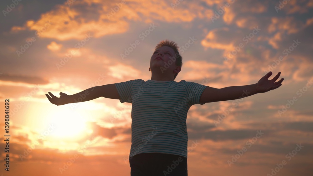 Child plays in park against sky. Little boy prays against background of sky and sun. Child raised his hands to sky in park at sunset, true faith. Religion and god, childhood dreams. Happy family Child plays in park against sky. Little boy prays against background of sky and sun. Child raised his hands to sky in park at sunset, true faith. Religion and god, childhood dreams. Happy family